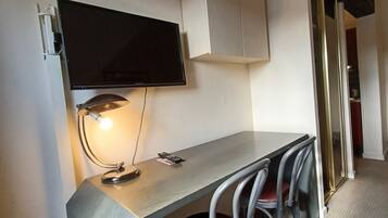 A compact room with a desk, a chair, a television mounted on the wall, and a cabinet.