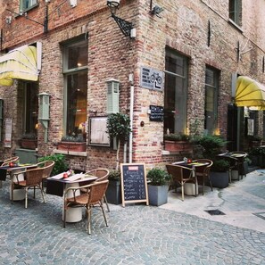 Un cafè a l'exterior amb parets de maó, cadires de vimetla i un menú a la pissarra.