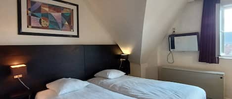 A hotel room with two beds, a framed abstract painting, a bedside lamp, a flat-screen TV, and a window with curtains.