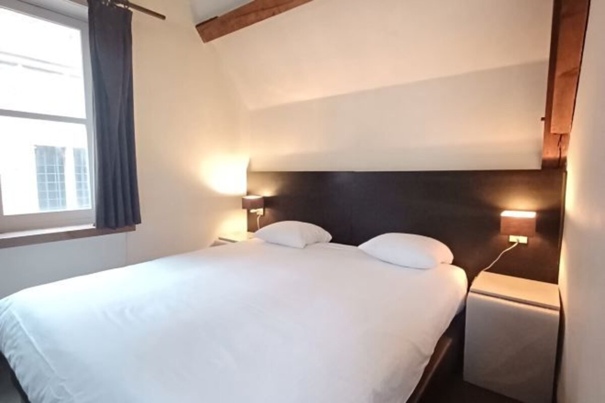 Een net opgemaakt bed met witte lakens in een hotelkamer.
