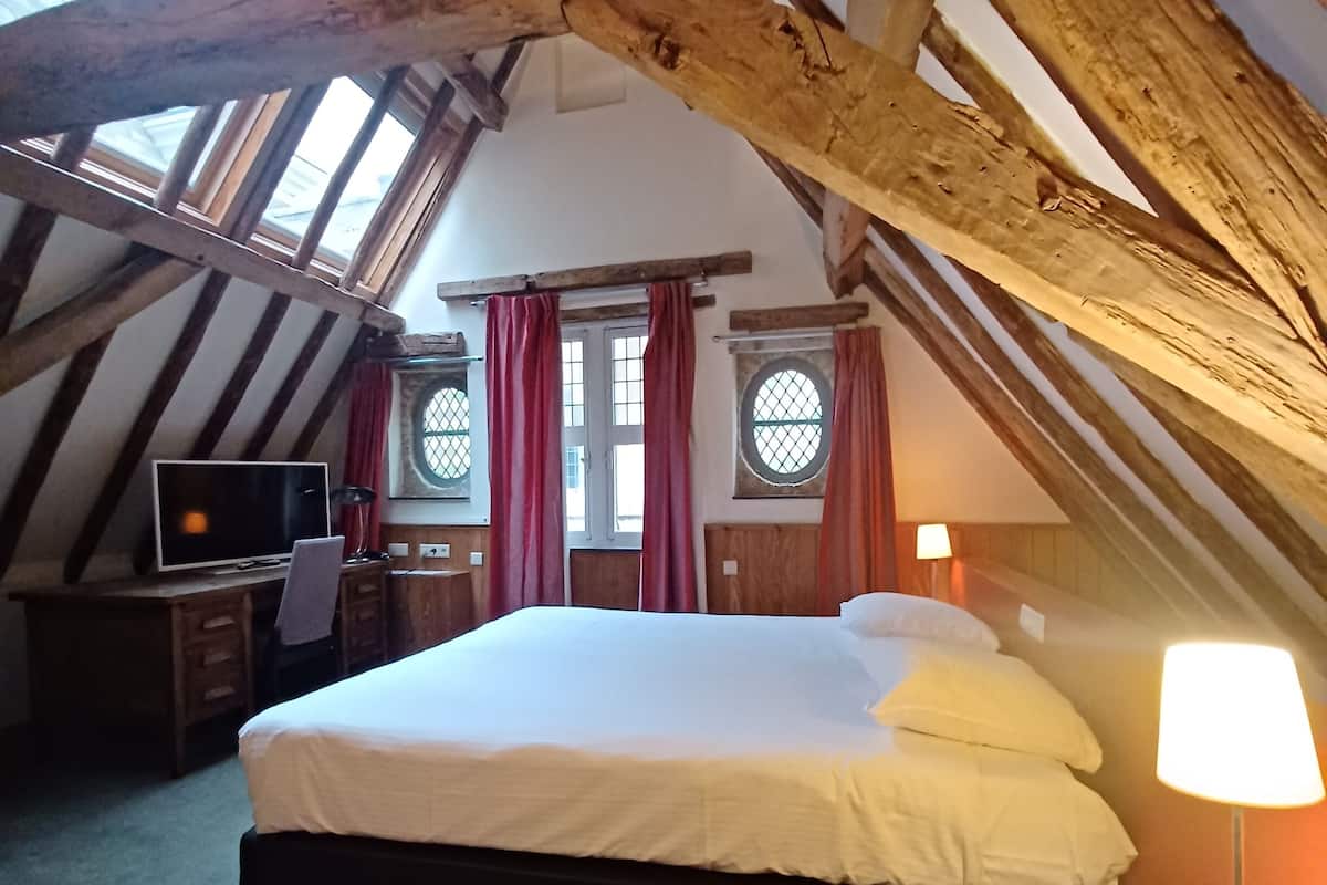Une chambre à coucher avec un grand lit, un bureau avec une chaise, une télévision et deux fenêtres avec des rideaux.