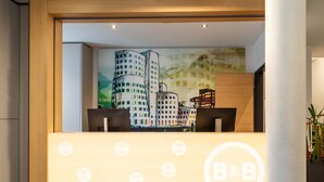 Un mostrador de recepción con un mural de la ciudad, el logotipo de un B&B y una planta a la derecha.