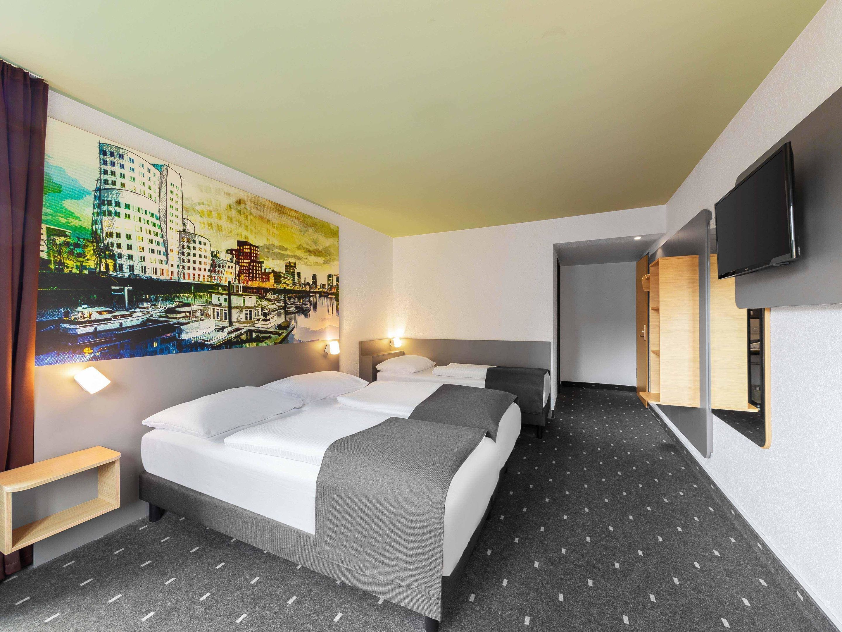Ein Hotelzimmer mit zwei Betten, einem Stadtbildgemälde, einem Fernseher und einem kleinen Holztisch.