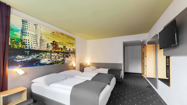 Habitación de hotel con dos camas, un cuadro de un paisaje urbano, un televisor y una mesita de madera.