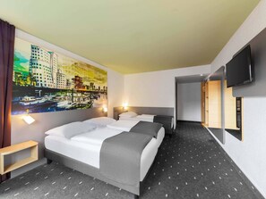 Habitación de hotel con dos camas, un cuadro de un paisaje urbano, un televisor y una mesita de madera.
