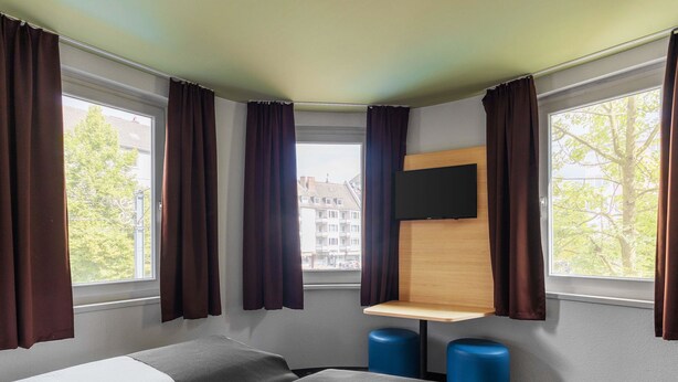 Una habitación de hotel con dos camas, un televisor montado en la pared y una mesita.