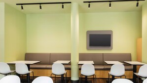 Un restaurante moderno con cabinas y mesas, un pilar grande y un televisor de pantalla plana en la pared.