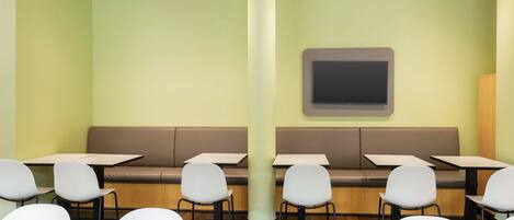 A modern restaurant with booths and tables, a large pillar, and a flat-screen TV on the wall.