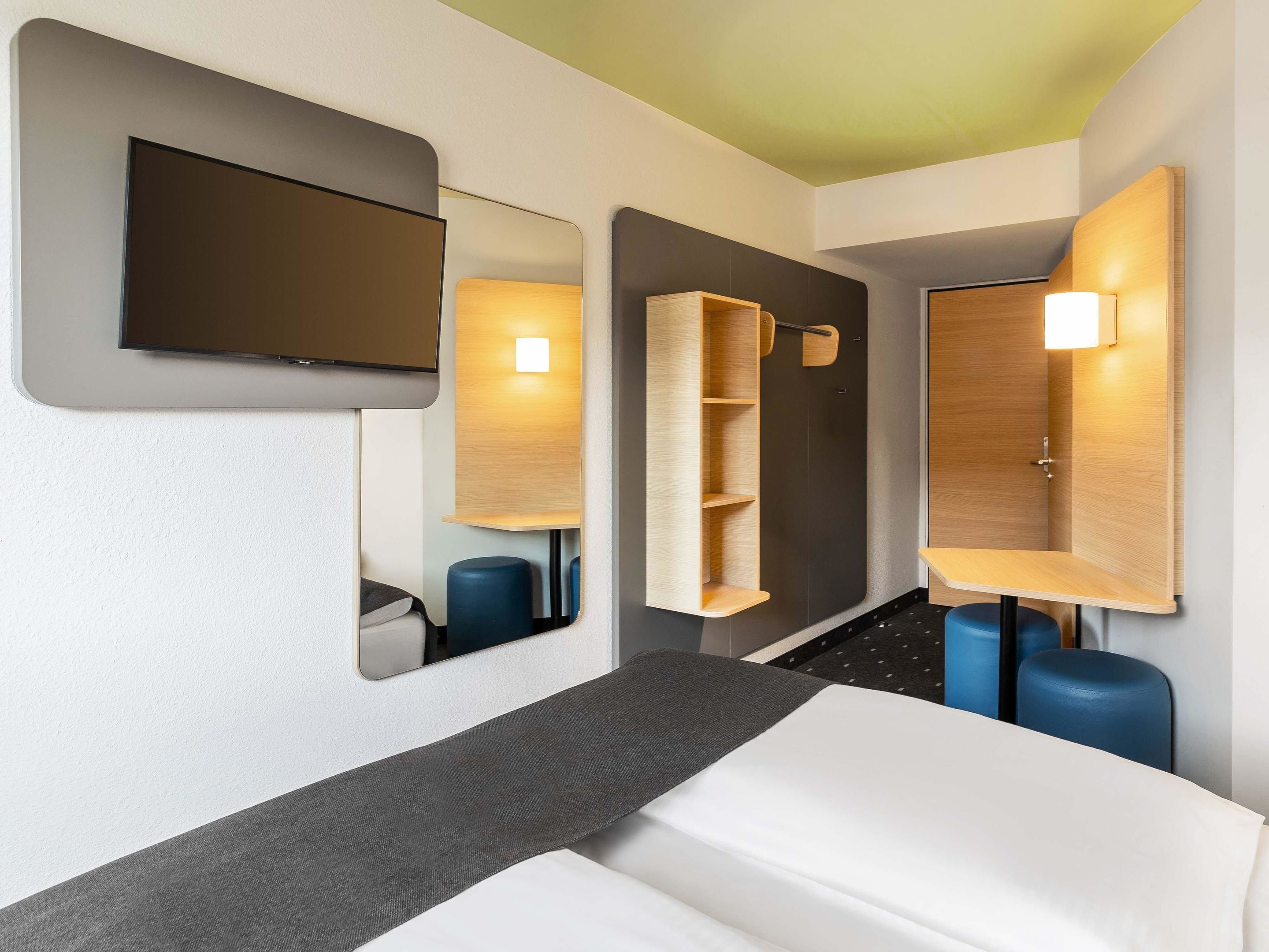 Ein modernes Hotelzimmer mit Bett, einem wandmontierten Flachbildfernseher und integrierten Regalen mit Spiegel.