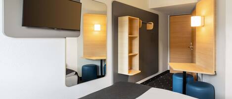Ein modernes Hotelzimmer mit Bett, einem wandmontierten Flachbildfernseher und integrierten Regalen mit Spiegel.