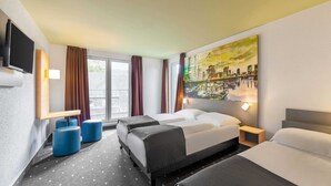 Habitación de hotel con dos camas, un televisor, un cuadro de paisaje urbano y una ventana con cortinas.
