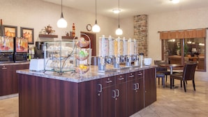 A kitchen area with a central island, beverage dispensers, and a seating area with chairs and a table. - Ramada by Wyndham Camrose (Camrose)