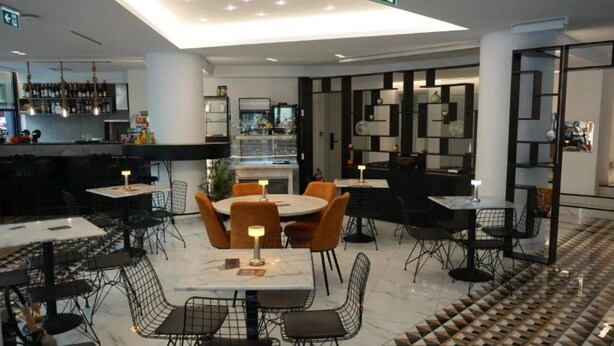 A modern restaurant with round tables, black chairs, and a patterned floor. - Athens Moka Hotel (Athens)