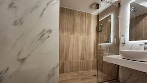 A bathroom with a glass-enclosed shower, a white sink, and marble walls. - Athens Moka Hotel (Athens)
