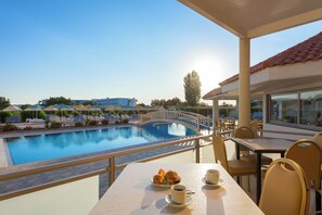 A poolside view with a dining area, a bridge over the pool, and a clear sky. - Memphis Hotel (Rhodes)