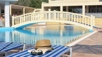 A pool area with lounge chairs, a bridge, and a building in the background.