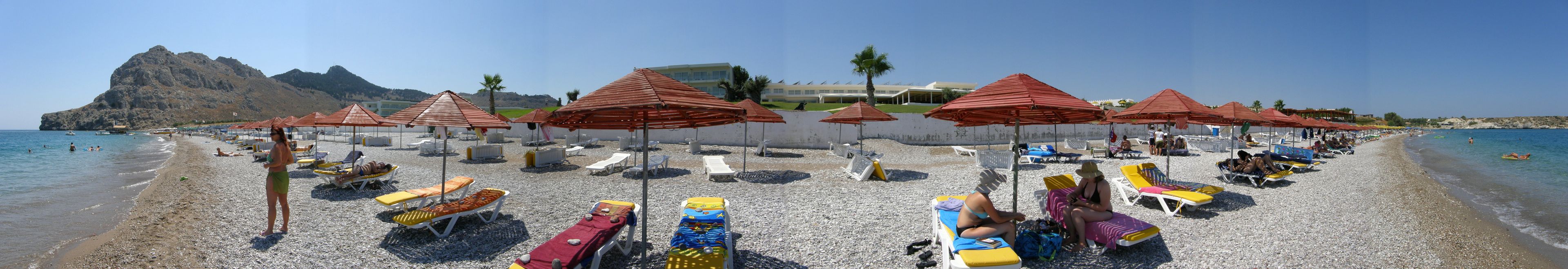 Una playa con tumbonas y sombrillas, un litoral rocoso y un edificio al fondo.