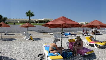Una playa con tumbonas y sombrillas, un litoral rocoso y un edificio al fondo.
