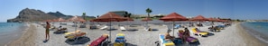 Une plage avec des transats et des parasols, une côte rocheuse et un bâtiment en arrière-plan.