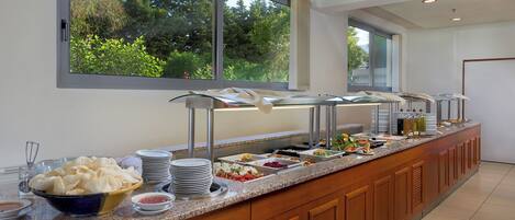 A buffet setup with various food items and a view of greenery outside.