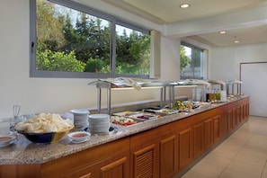 A buffet setup with various food items and a view of greenery outside. - Memphis Hotel (Rhodes)