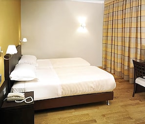 Una habitación de hotel con cama, lámparas de noche, teléfono y una silla.