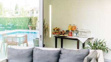 Ein modernes Wohnzimmer mit Blick auf einen Pool, einem Essbereich mit Obst und Getränken und einer gemütlichen Sitzecke.