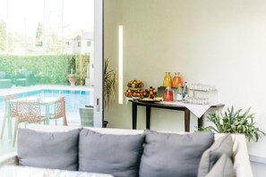 Una sala de estar moderna con vista a la piscina, un comedor con frutas y bebidas, y un espacio de descanso acogedor.
