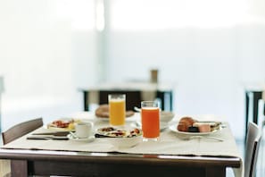 Une table de petit-déjeuner avec des assiettes remplies de nourriture, un verre de jus d’orange et un verre de lait.