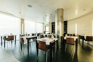 A modern dining area with multiple tables and chairs, a central pillar, and a view of the outside.