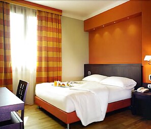Habitación de hotel con cama, escritorio, silla, mesita de noche y lámpara.