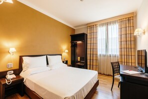Una habitación de hotel con cama, mesita de noche, lámpara y escritorio con silla.