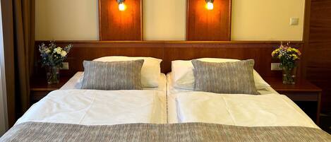 Una cama doble con dos almohadas, cabecera de madera y dos apliques.