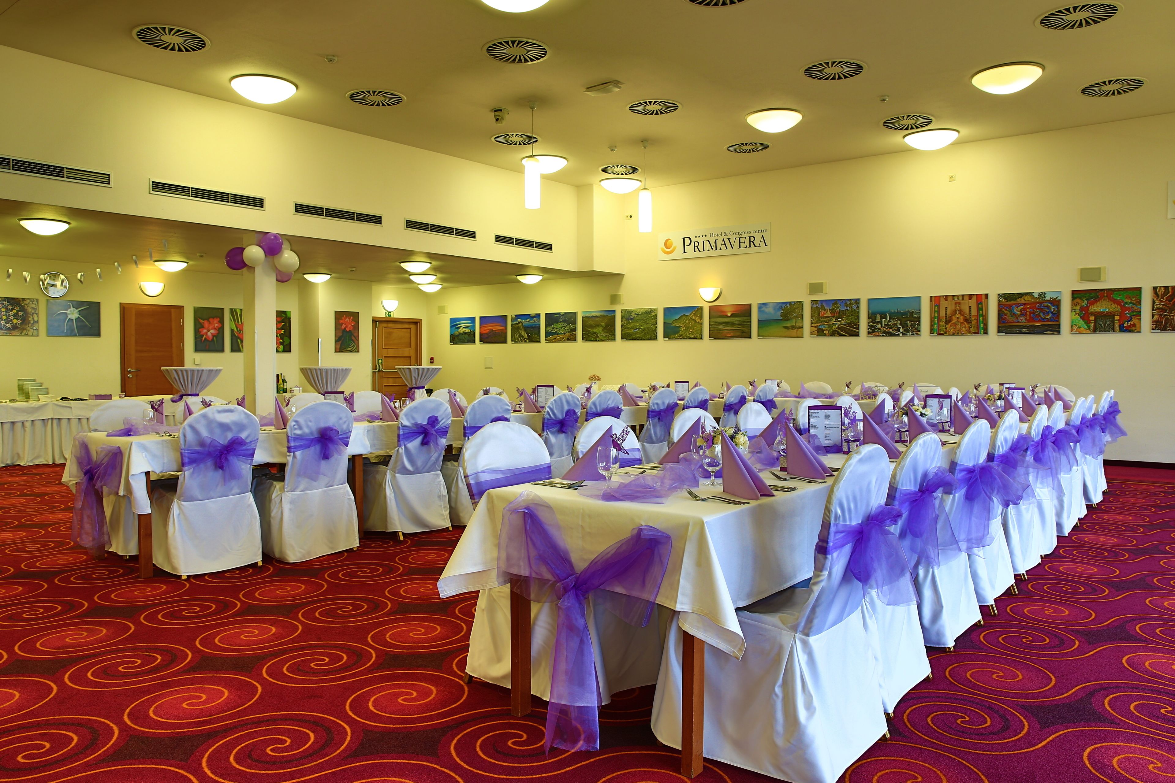 A banquet hall with tables set for a formal event, featuring purple sashes and white tablecloths.