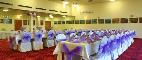 Un salón de banquetes con mesas dispuestas para un evento formal, con cintas moradas y manteles blancos.