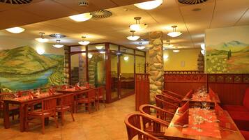A restaurant with wooden tables and chairs, a stone pillar, and a mural of a mountain landscape.