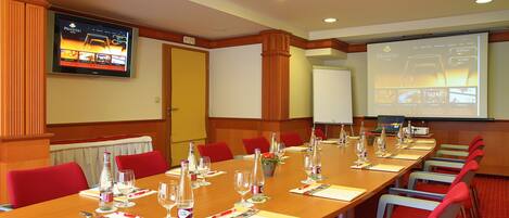 Un salón de conferencias con una larga mesa dispuesta para una reunión, equipado con sillas, botellas de agua y vasos.