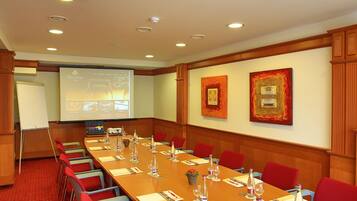 A conference room with a long table, red chairs, a projector screen, and framed artwork on the walls.