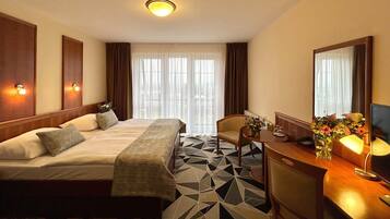 Une chambre d’hôtel avec un lit, un bureau et une chaise, un miroir et une fenêtre avec des rideaux.