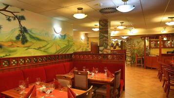 Un restaurant avec des banquettes rouges, des tables en bois et une fresque représentant un paysage.
