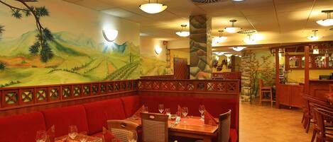 Un restaurante con asientos tapizados en rojo, mesas de madera y un mural con un paisaje.