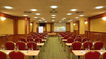 Una sala conferenze con file di sedie rosse, tavoli e uno schermo per proiezioni nella parte anteriore.