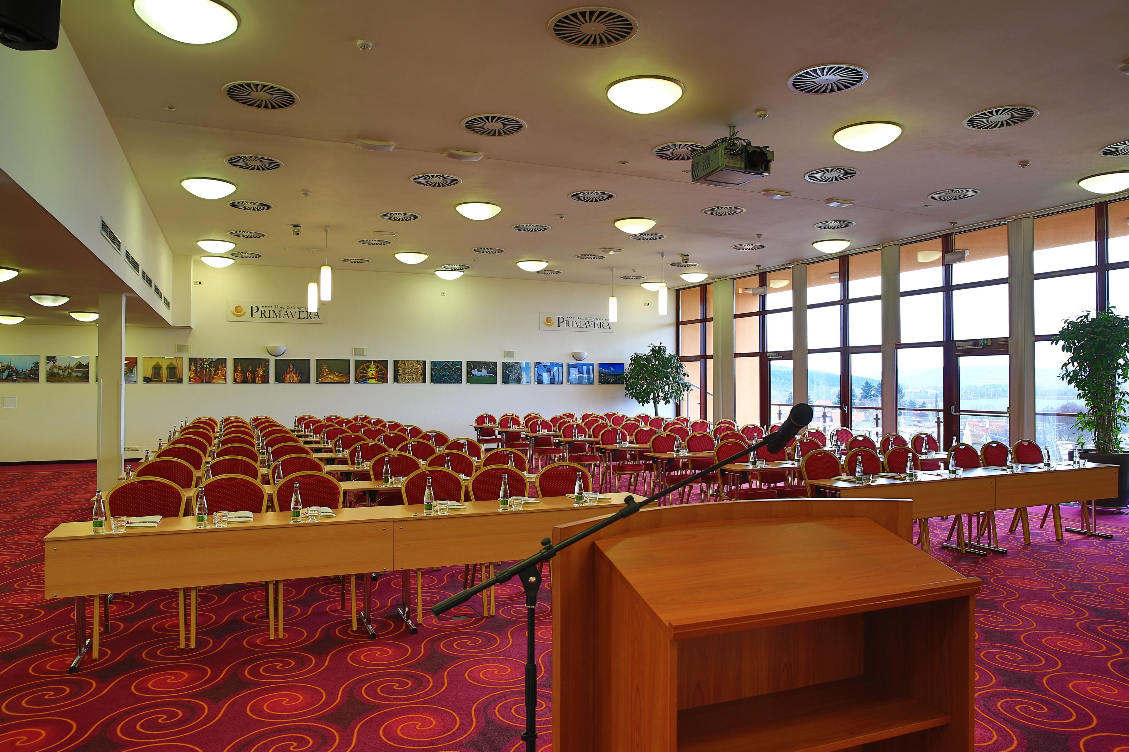 Konferenssitila, jossa on riveissä punaisia tuoleja, puhujapönttö ja matolla peitetty lattia.