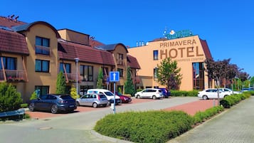 A hotel with a sign reading "Primavera Hotel & Congress Center" with multiple cars parked in front.