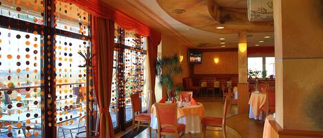 A restaurant with a dining area featuring round tables and chairs, a large window with a view of the street, and a ceiling with a floral design.