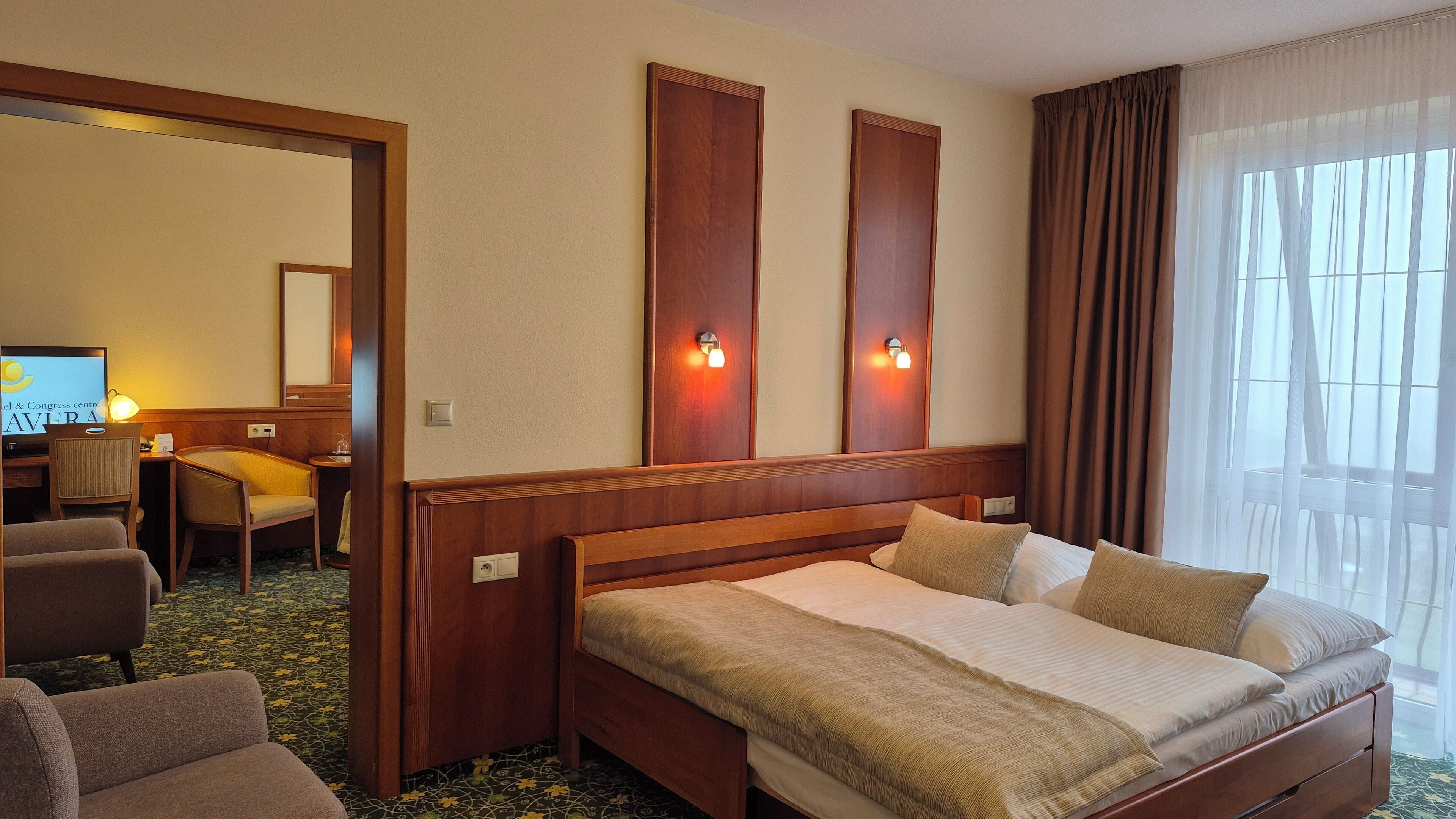 Habitación de hotel con cama, escritorio y silla. Hay dos luces fijadas a la pared sobre la cama.