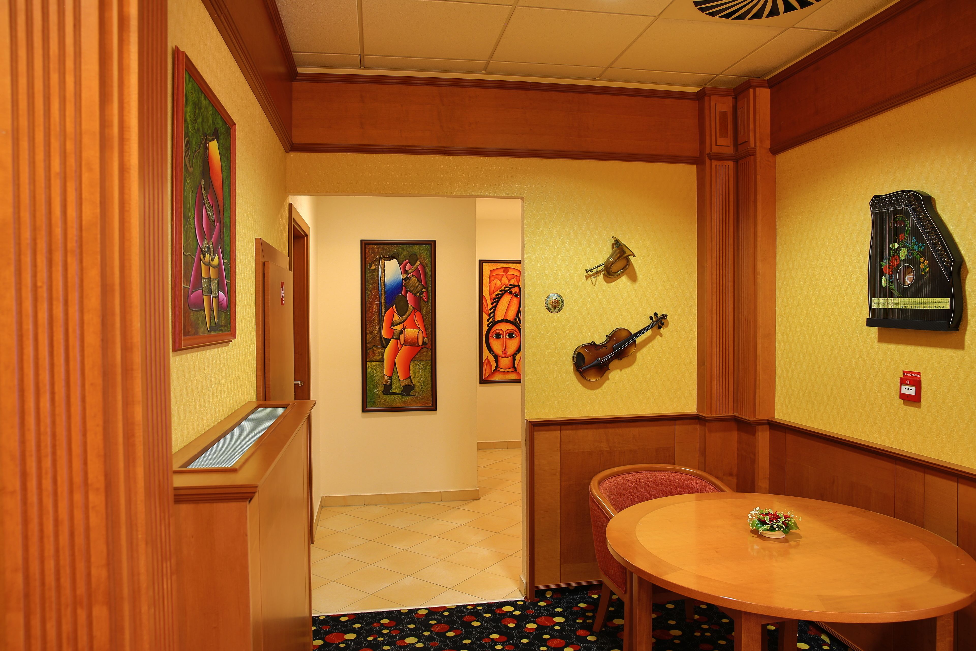 A hotel room with a wooden panel wall, a round table with a vase, and a violin on the wall.