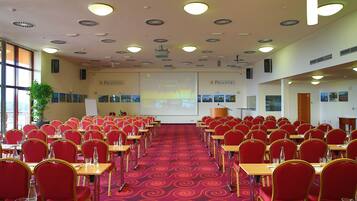 Una sala conferenze con file di sedie rosse e tavoli, uno schermo per proiettore e un pavimento rivestito di moquette.