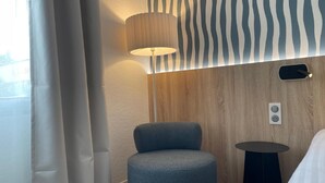 A modern hotel room with a round blue chair, a small black side table, a lamp, and a wooden accent wall. - Best Western Le Clos de l'Aube Rouge (Castelnau-le-Lez)