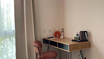 Een hotelkamer met een bed, een bureau met stoel, een koffiezetapparaat en een prullenbak.